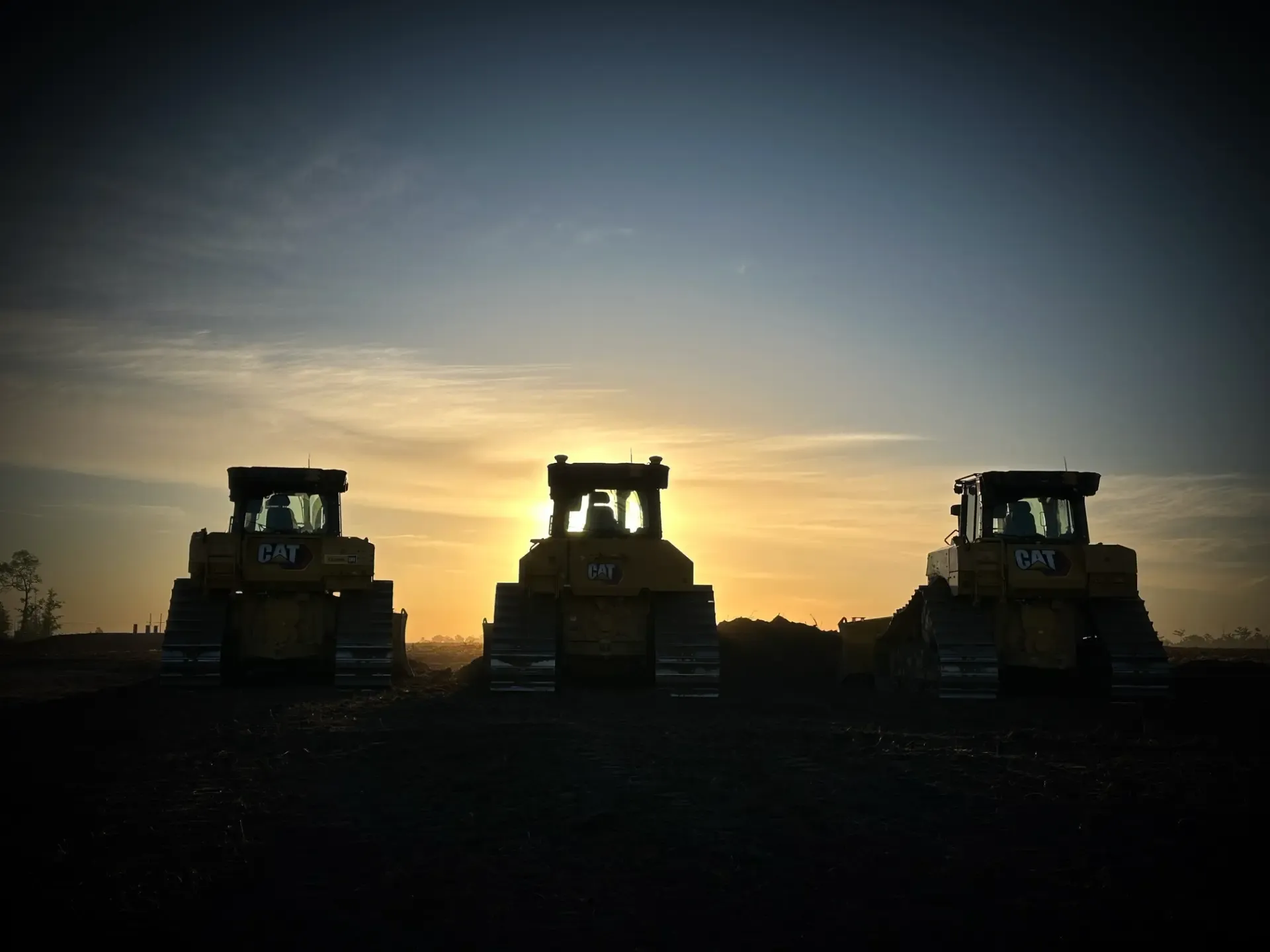 Silhouetted bulldozers at sunset in field