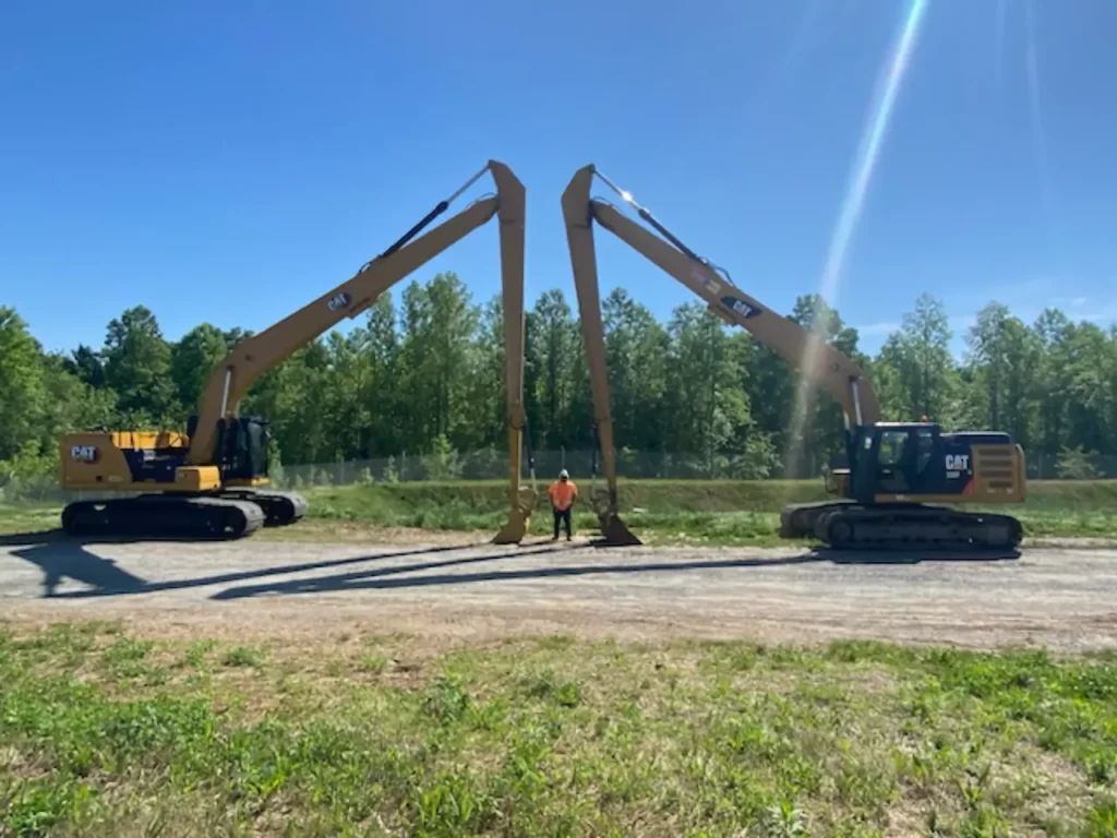 Worker between two extended excavator arms on sunny day
