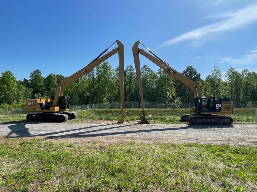 Two CAT excavators with extended booms on a clear day