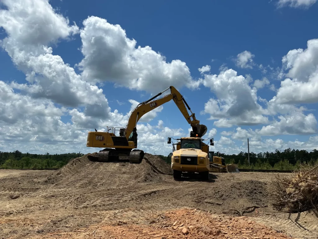 Excavator loading dirt into dump truck under cloudy sky