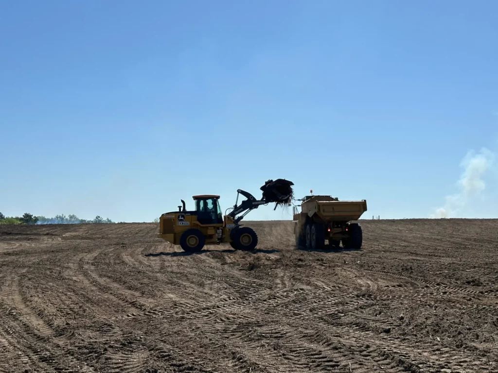 Bulldozer loading dirt into dump truck on field