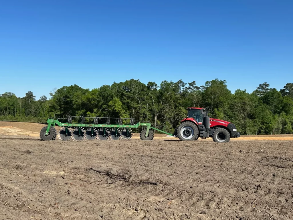 Red tractor plowing field with attached green equipment