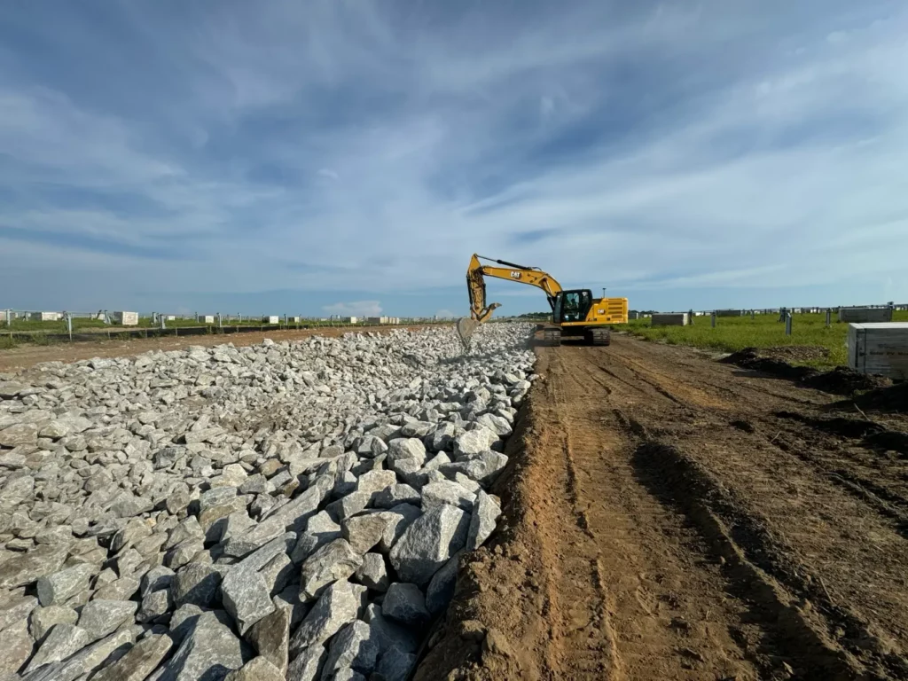 Excavator moving rocks at construction site under blue sky