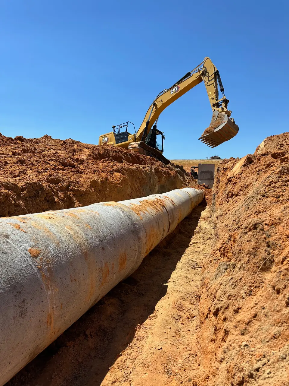Excavator working on laying large pipeline in trench